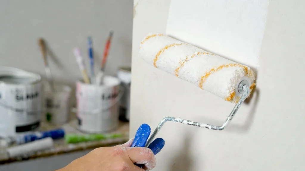 Primer plano de rodillo aplicando pintura en una pared durante un trabajo de pintor.